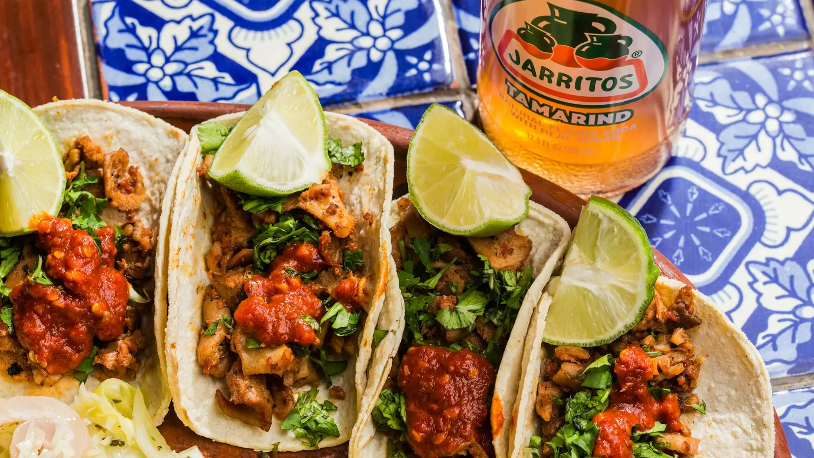 Street tacos with lime and a Jarritos soda on a hand-painted talavera tile table